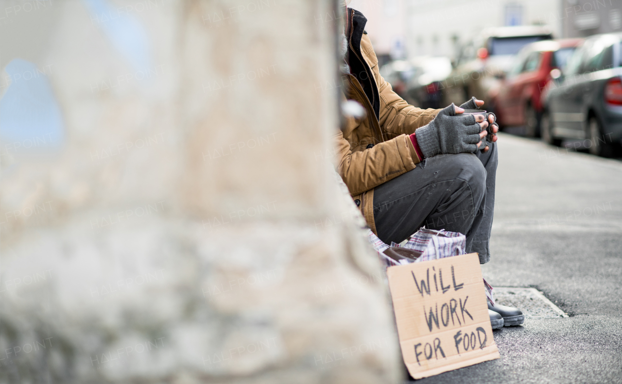 A midsection view of homeless beggar man with a carboard sign sitting outdoors in city asking for money donation. Copy space.