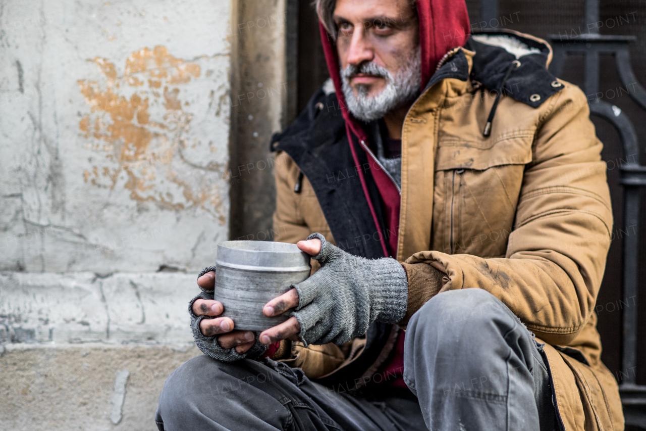 A homeless beggar man sitting in front of wooden gate outdoors in city asking for money donation.