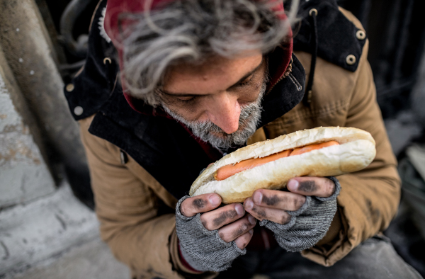 A top view of homeless beggar man outdoors in city, holding hot-dog. A close up.