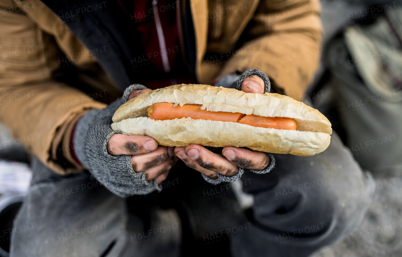 A midsection view of homeless beggar man outdoors in city, holding hot-dog. A close up.