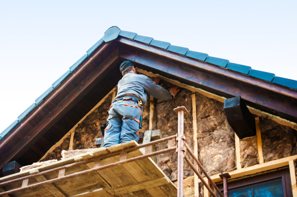 Construction worker standing on scaffold thermally insulating house facade with glass wool.