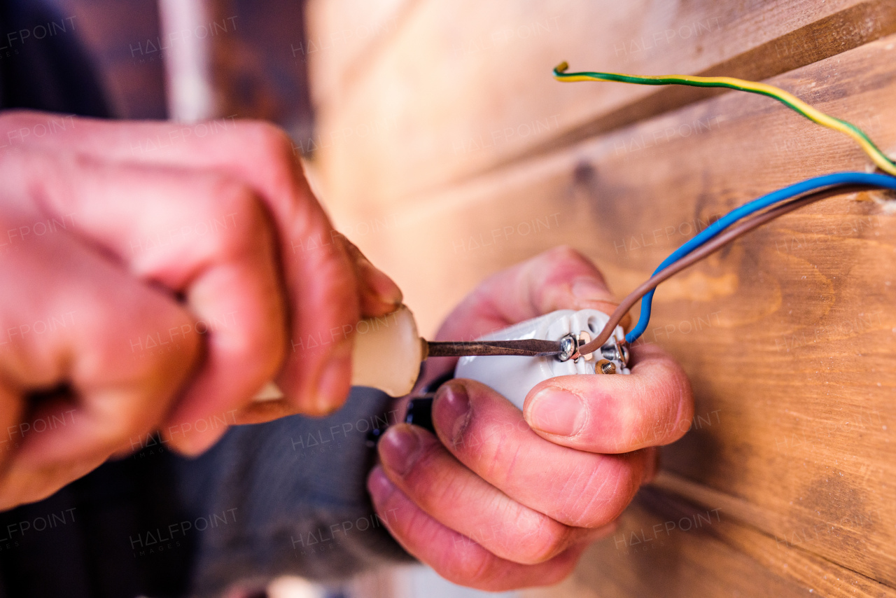 Hands of unrecognizable electrician working with screwdriver, wooden wall