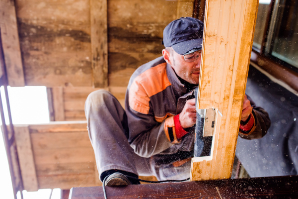 Carpenter with grinder. Man grinding planks of wood for home construction.