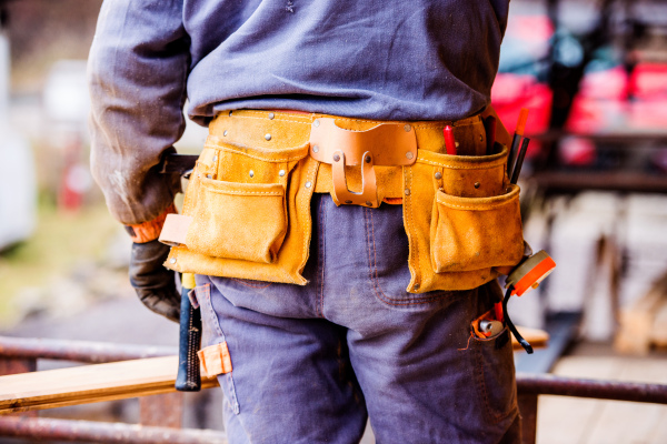 Close up of unrecognizable construction worker with tool bag on site, rear view