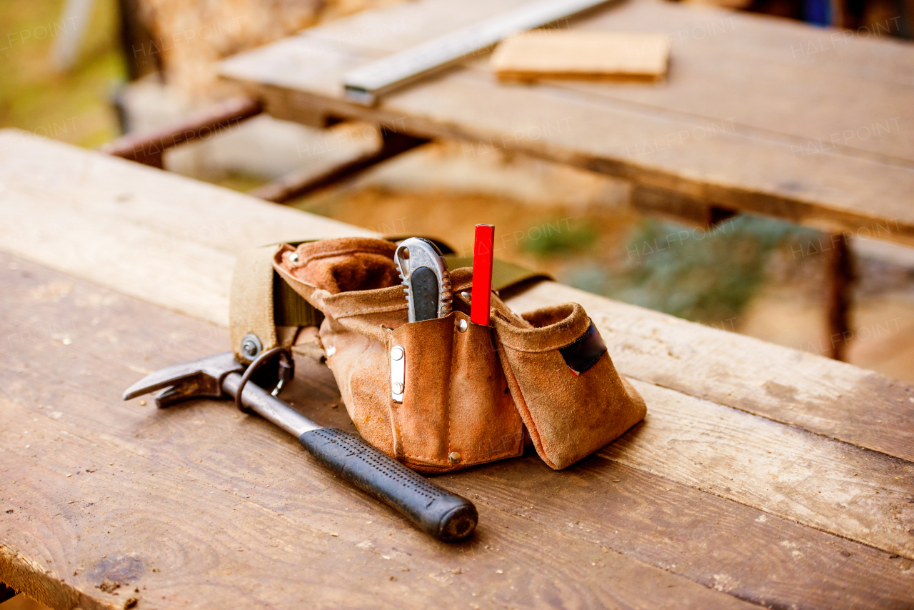 Carpenters bag with belt full of tools laid on wooden table. Construction site.