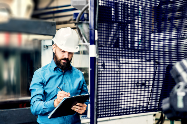 A portrait of a mature industrial man engineer with clipboard in a factory, working. Copy space.