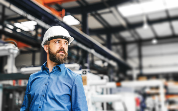 A portrait of a happy industrial man engineer with helmet in a factory. Copy space.