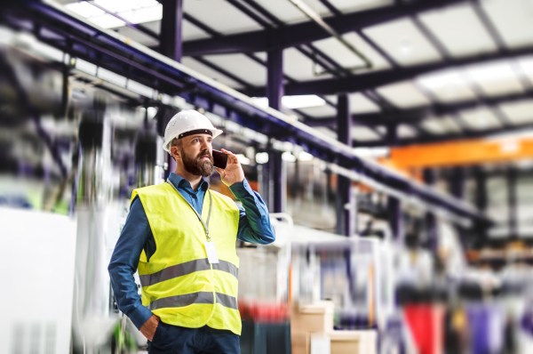 A portrait of a mature industrial man engineer with smartphone in a factory, making a phone call.