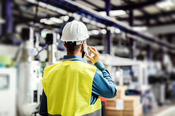 A rear view of a mature industrial man engineer with smartphone in a factory, making a phone call.