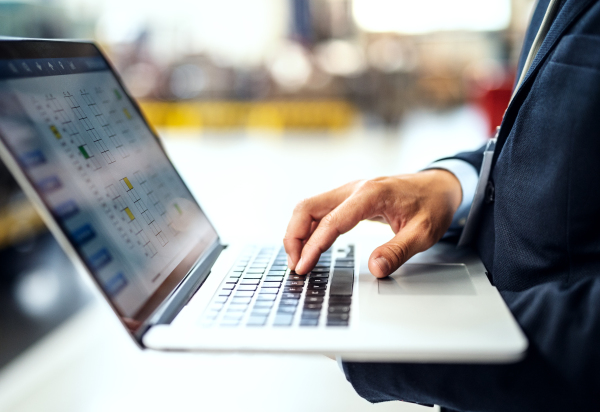 A midsection view of unrecognizable industrial man engineer standing in a factory with laptop, typing.