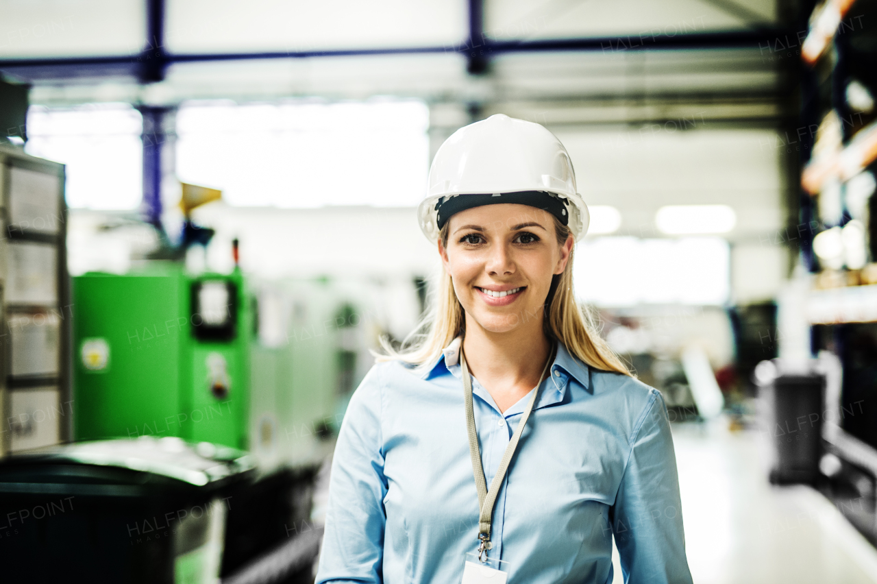 A portrait of a young industrial woman engineer with white helmet standing in a factory.