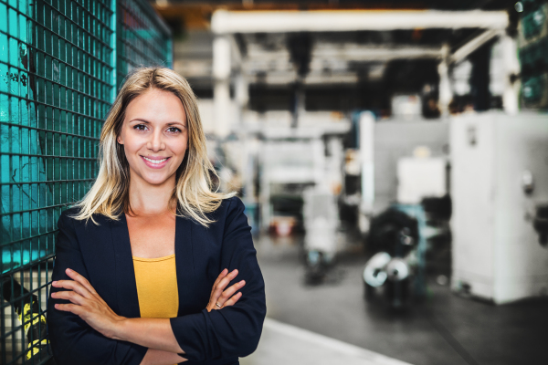 A portrait of a young industrial woman engineer standing in a factory, arms crossed. Copy space.