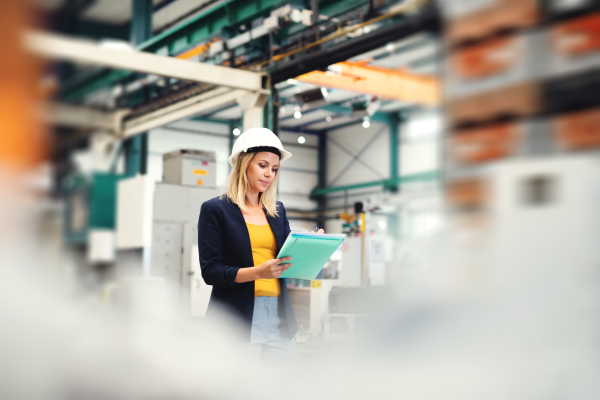 A portrait of a young industrial woman engineer in a factory, checking something.