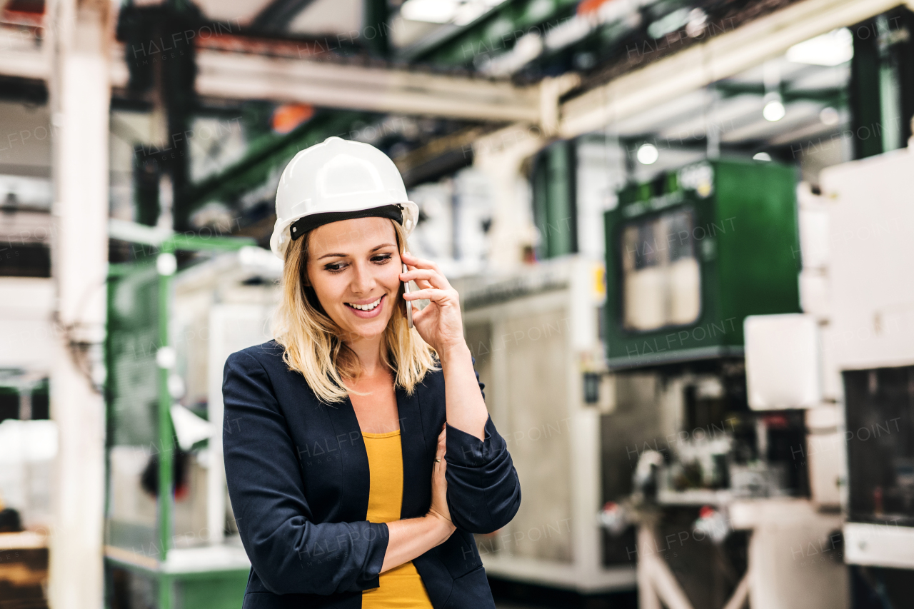 A portrait of a happy industrial woman engineer on the phone, standing in a factory.