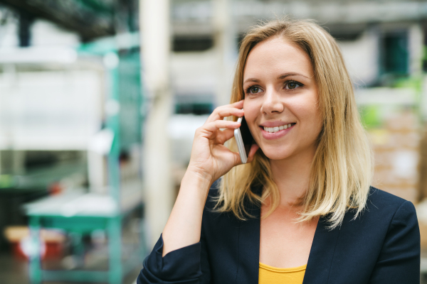 A portrait of a happy industrial woman engineer on the phone, standing in a factory.