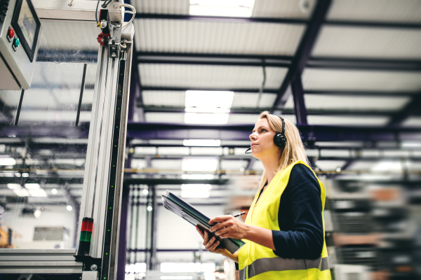 A portrait of a young industrial woman engineer with headset and clipboard in a factory, working.