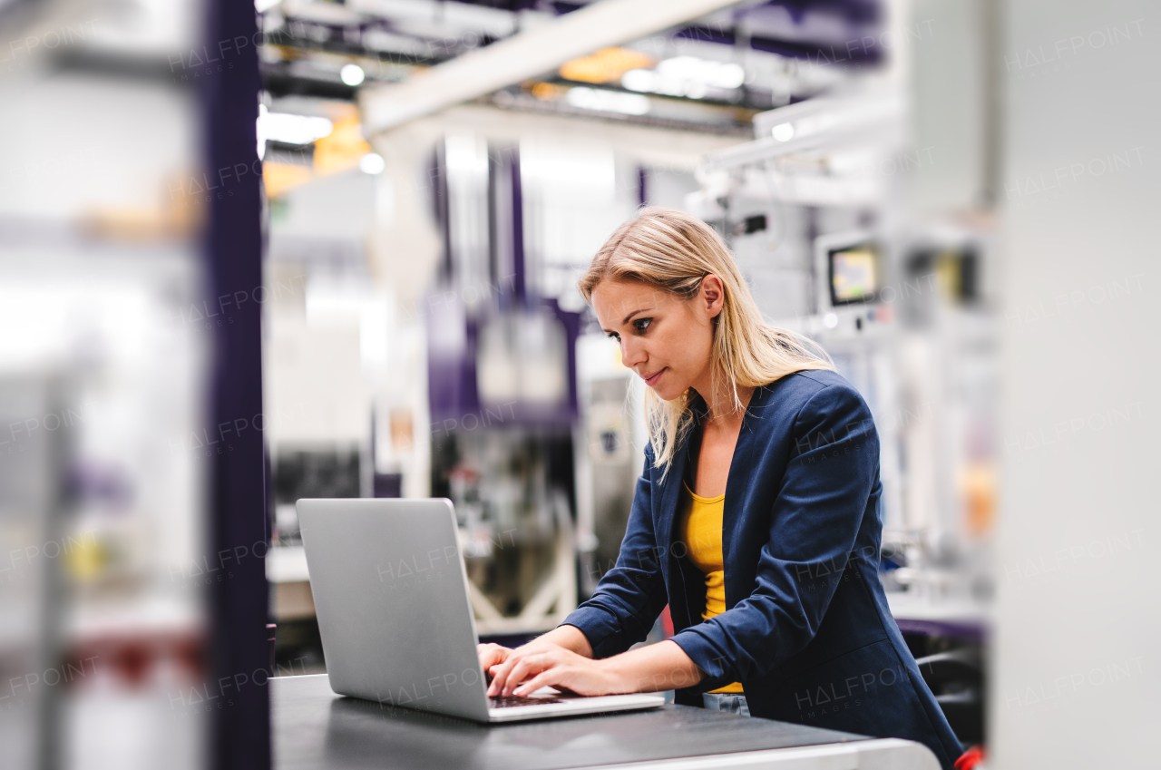 A portrait of a young industrial woman engineer in a factory, using laptop.