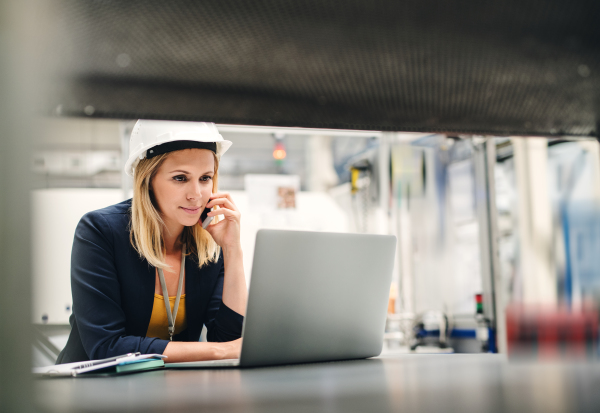 An industrial woman engineer in a factory using laptop and smartphone.