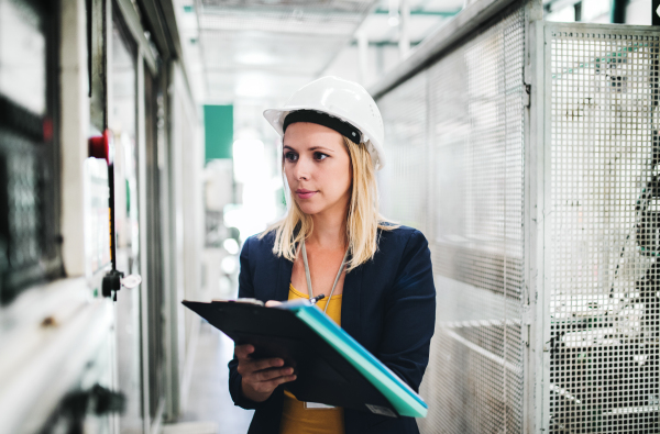 A portrait of a young industrial woman engineer in a factory, writing.