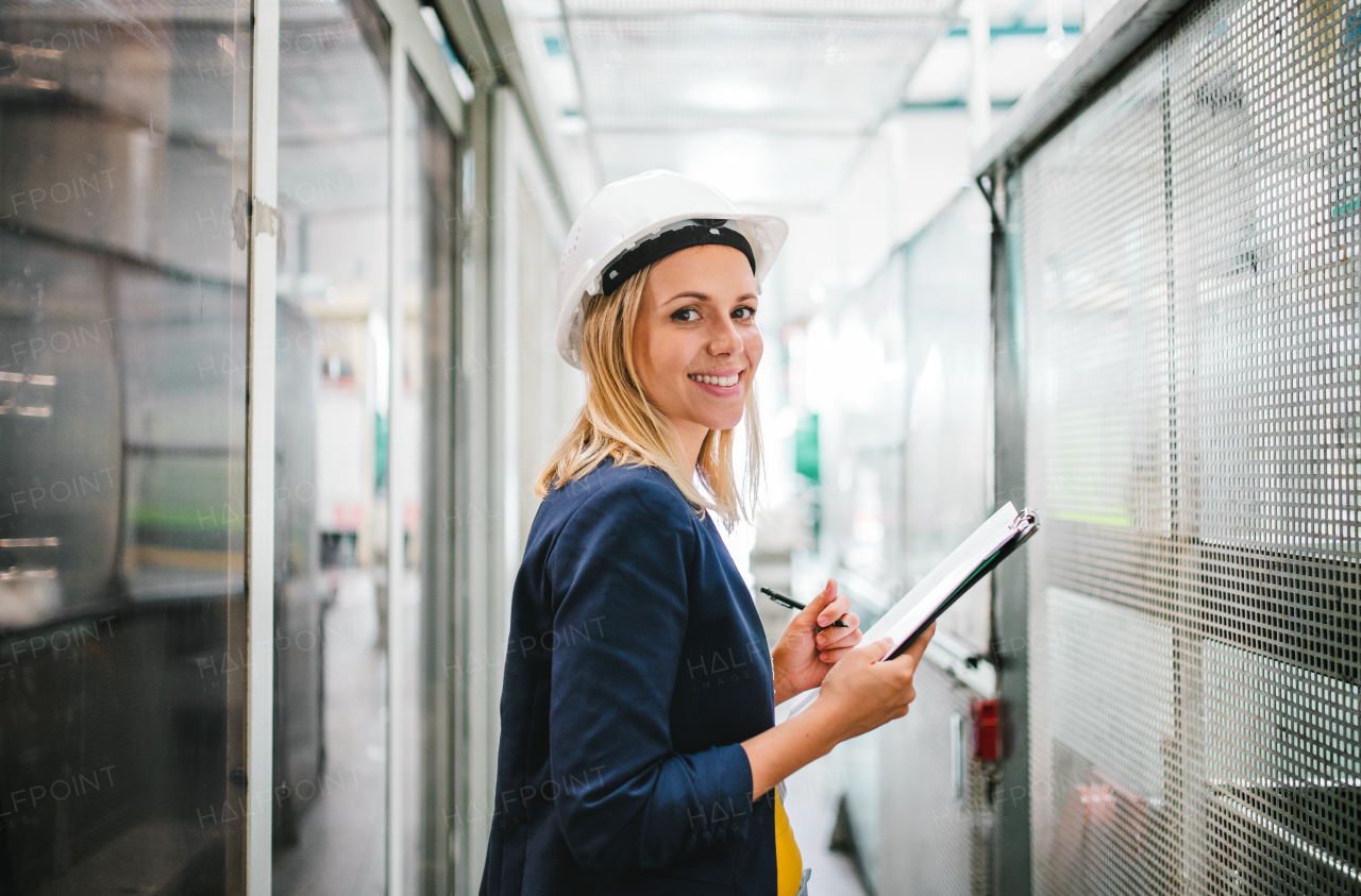 A portrait of a young industrial woman engineer in a factory checking something.