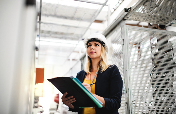 A portrait of a young industrial woman engineer in a factory checking something.