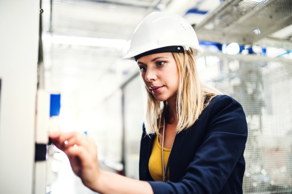 A portrait of a young industrial woman engineer in a factory checking something.