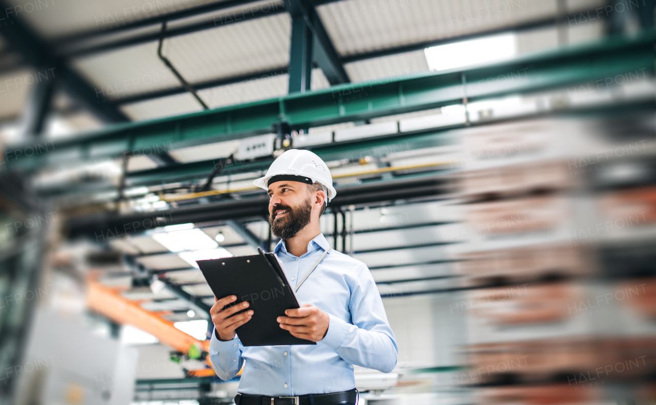 A portrait of a mature industrial man engineer with clipboard standing in a factory. Copy space.