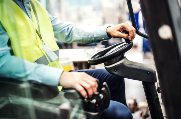 Unrecognizable industrial man engineer or driver sitting in a forklift in a factory.