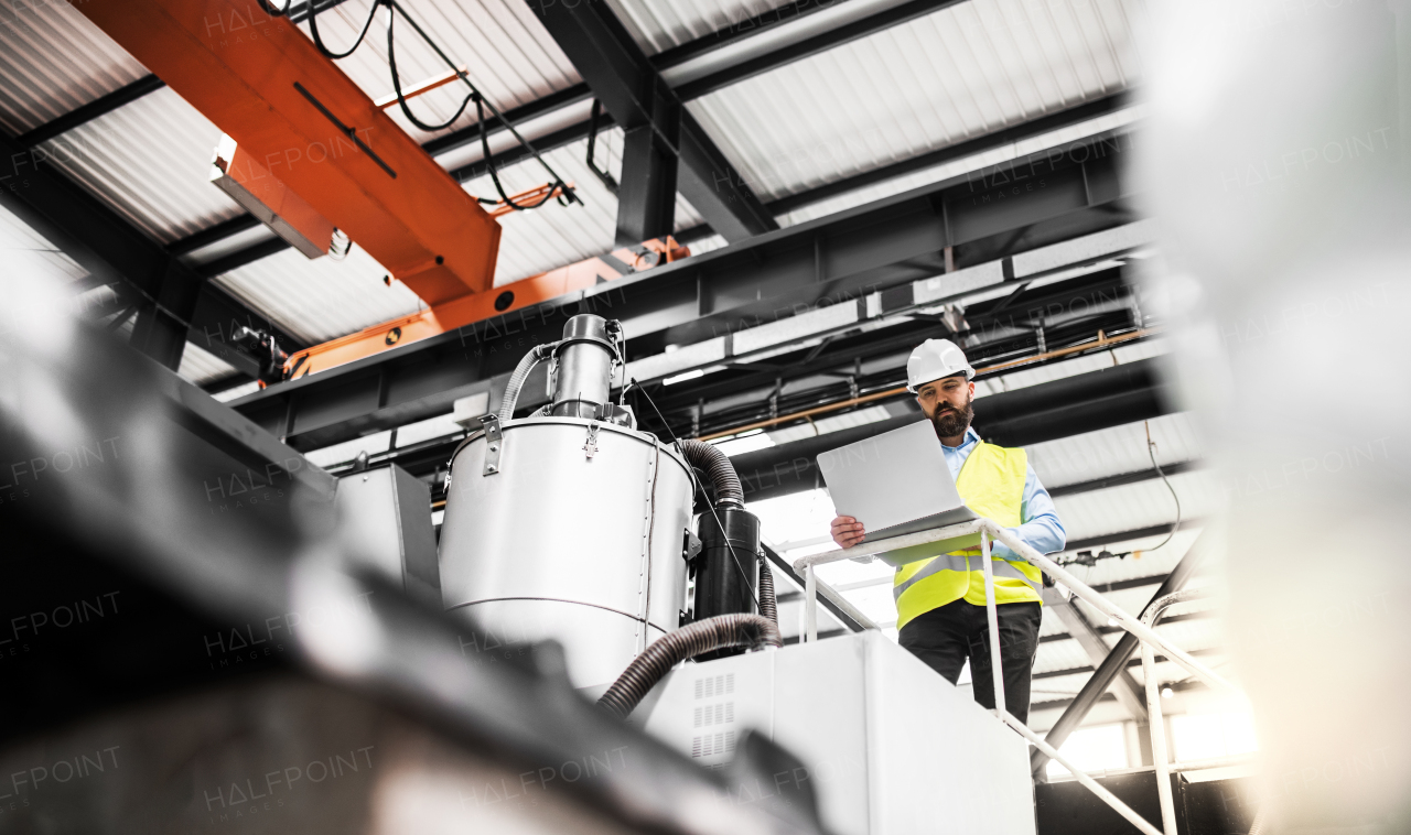 A low angle view of a mature industrial man engineer with laptop in a factory, working.