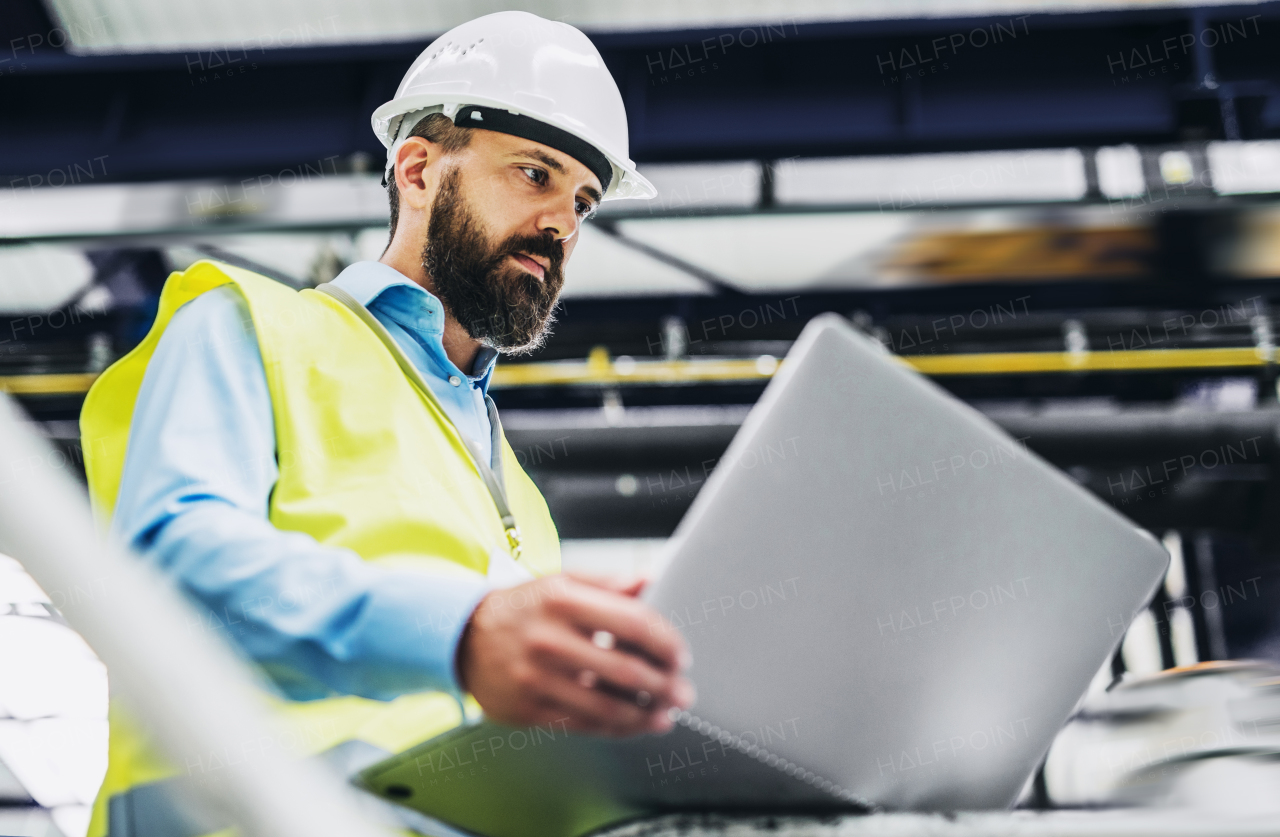 A portrait of a mature industrial man engineer with laptop in a factory, working.