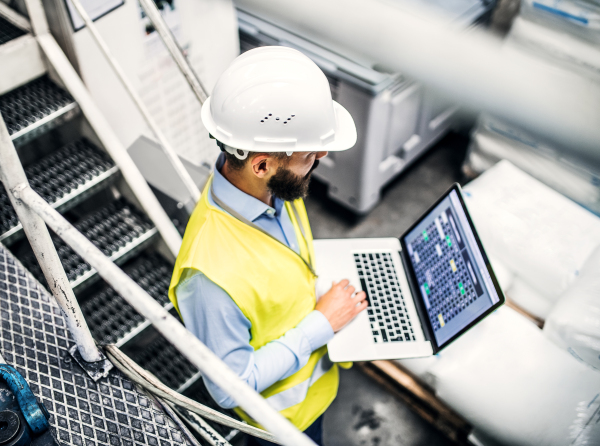 A portrait of a mature industrial man engineer with laptop in a factory, working. High-angle view.