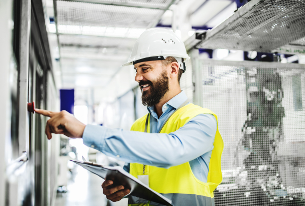 A portrait of a mature industrial man engineer with clipboard in a factory, working. Copy space.