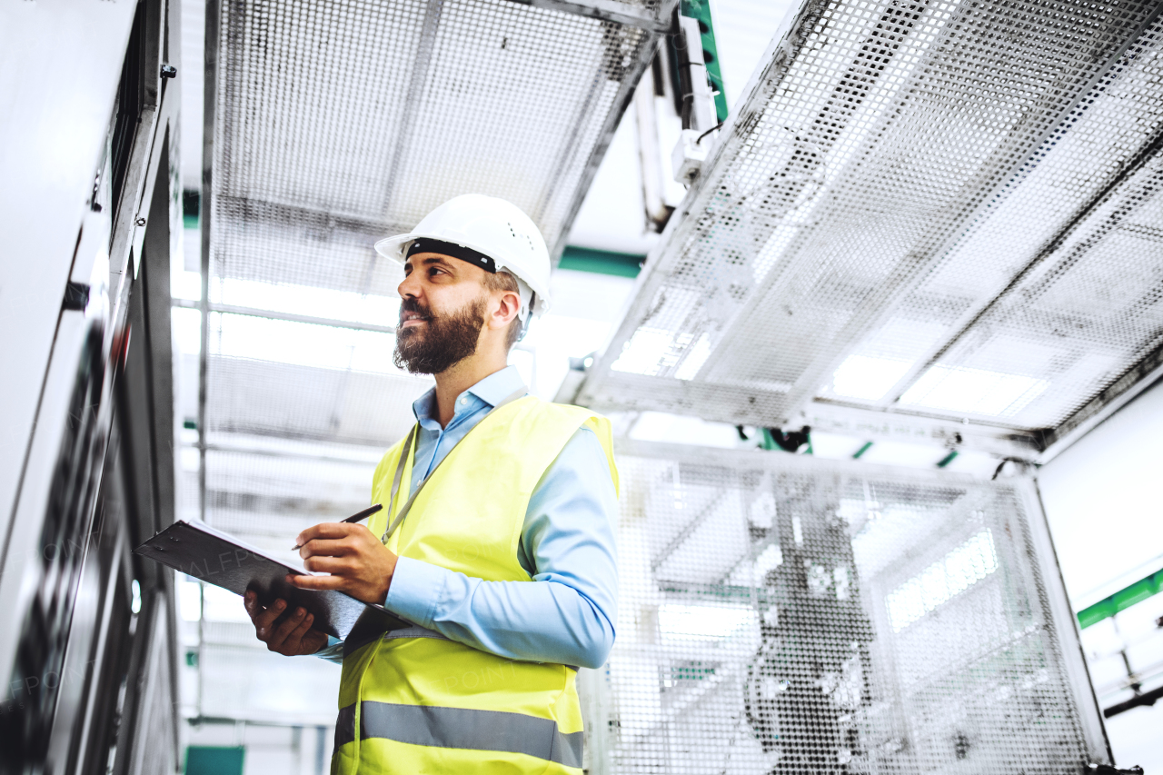 A portrait of a mature industrial man engineer with clipboard in a factory, working. Copy space.