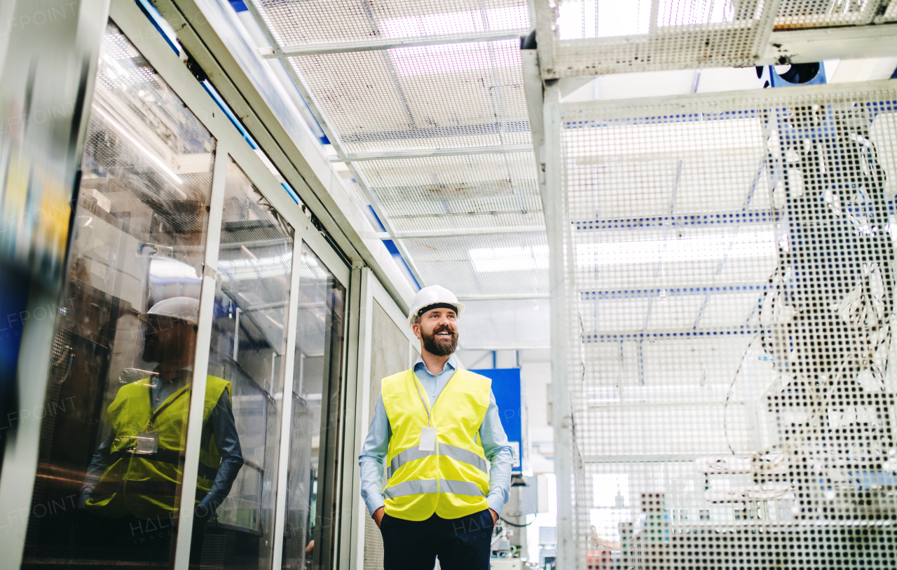 A portrait of a happy industrial man engineer in a factory, hands in pockets. Copy space.