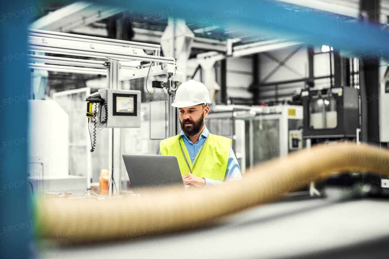 A portrait of a mature industrial man engineer with laptop in a factory, working.