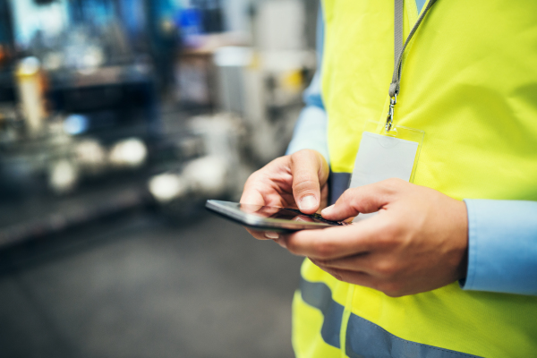 An unrecognizable industrial man engineer with name tag in a factory, using smartphone. Copy space.