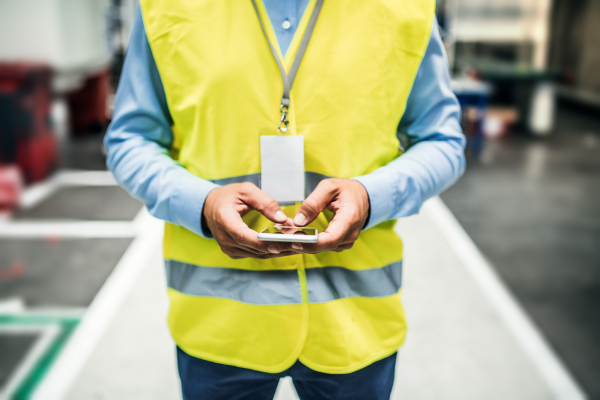 An unrecognizable industrial man engineer with name tag in a factory, using smartphone. Copy space.