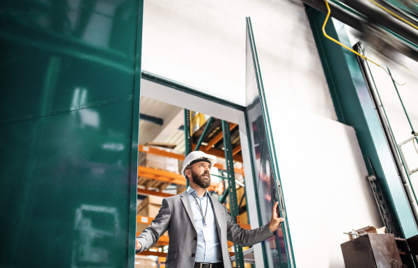 An industrial man engineer with a jacket in a factory, opening and going through the gate.