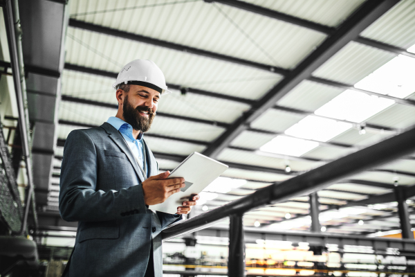 A portrait of a mature industrial man engineer with tablet in a factory. Copy space.