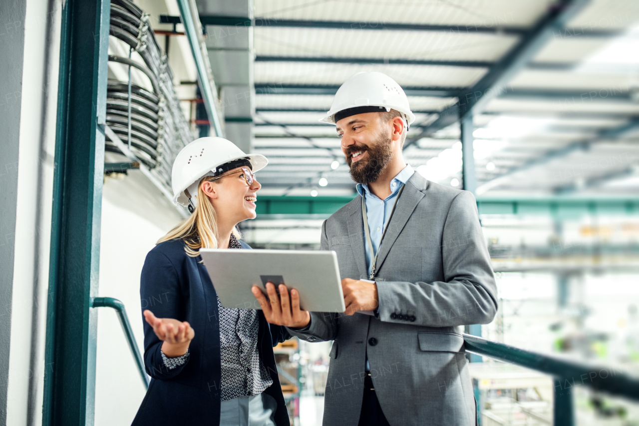 A portrait of a mature industrial man and woman engineer with tablet in a factory, working.