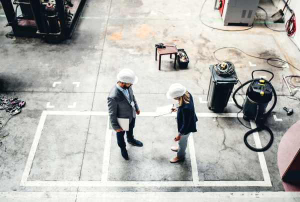 A high angle view of an industrial man and woman engineer with tablet in a factory, working.