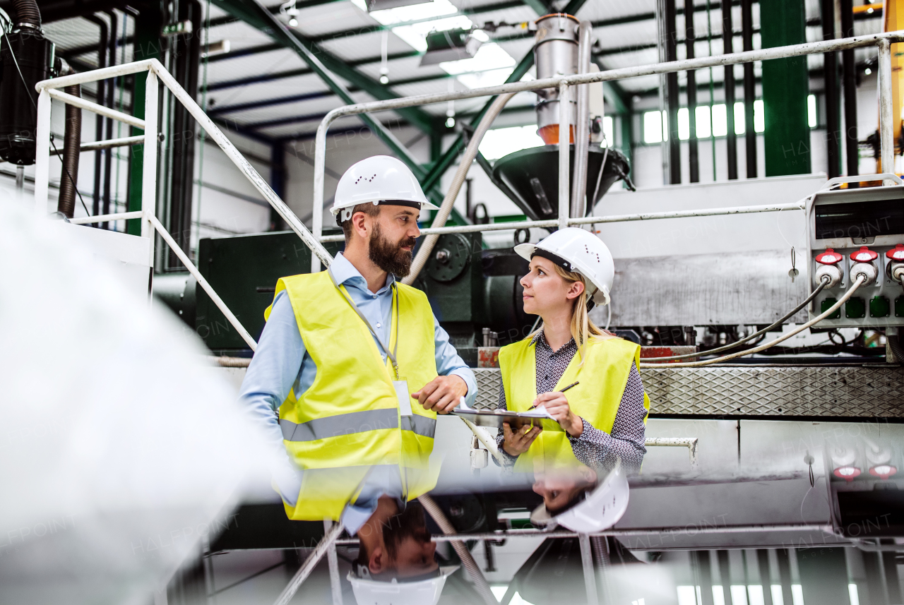 A portrait of a mature industrial man and woman engineer with clipboard in a factory, working.