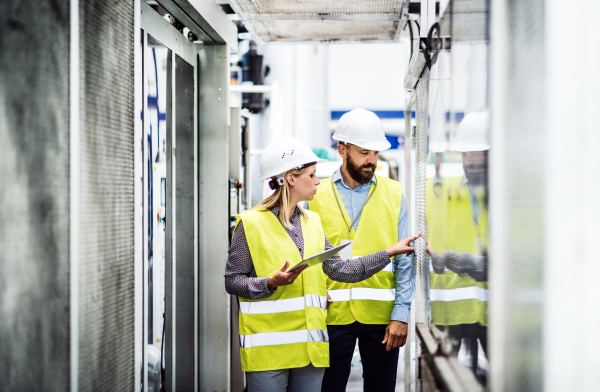 A portrait of a mature industrial man and woman engineer with tablet in a factory, working.