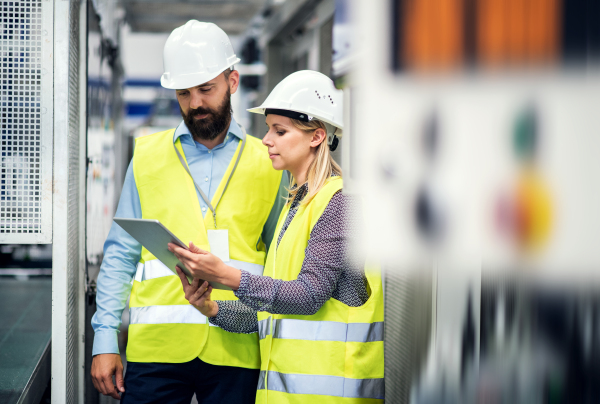 A portrait of a mature industrial man and woman engineer with tablet in a factory, talking.