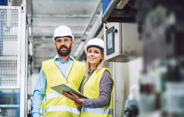 A portrait of a mature industrial man and woman engineer with tablet in a factory. Copy space.