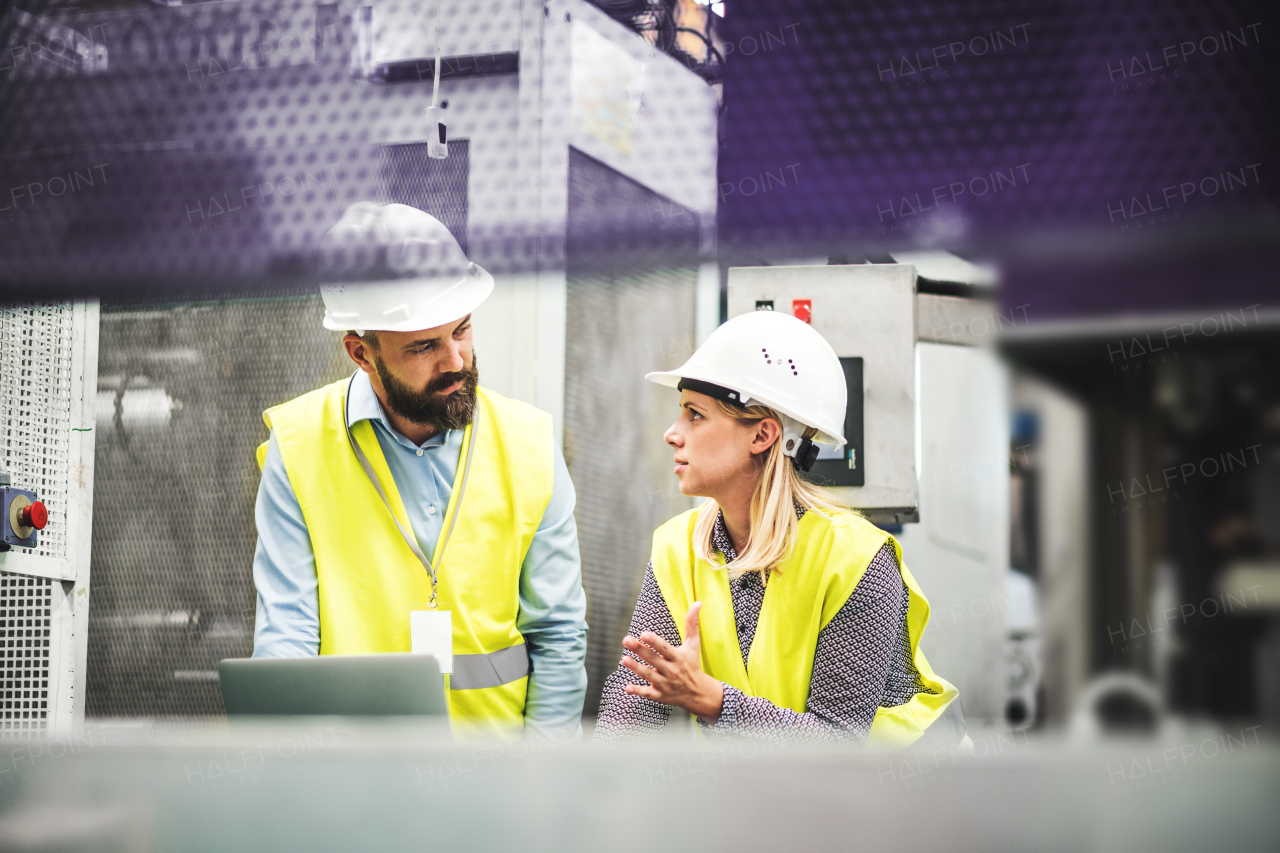 A portrait of a mature industrial man and woman engineer with laptop in a factory, working.