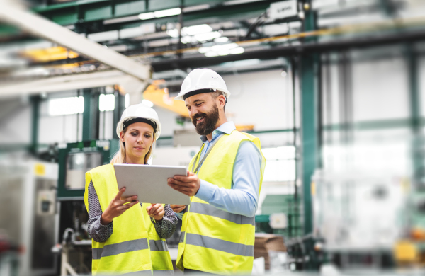 A portrait of a mature industrial man and woman engineer with tablet in a factory, talking.