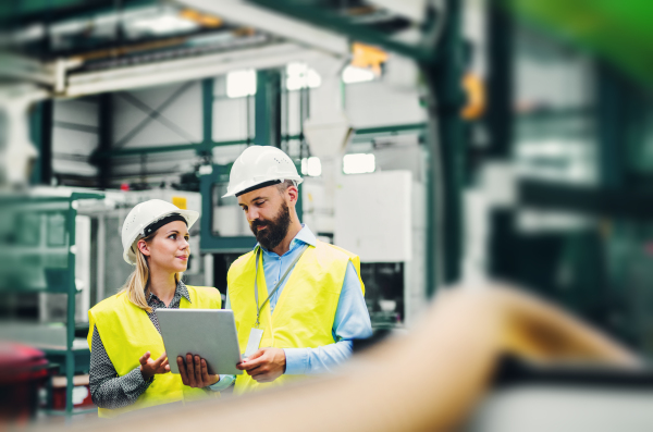 A portrait of a mature industrial man and woman engineer with tablet in a factory. Copy space.