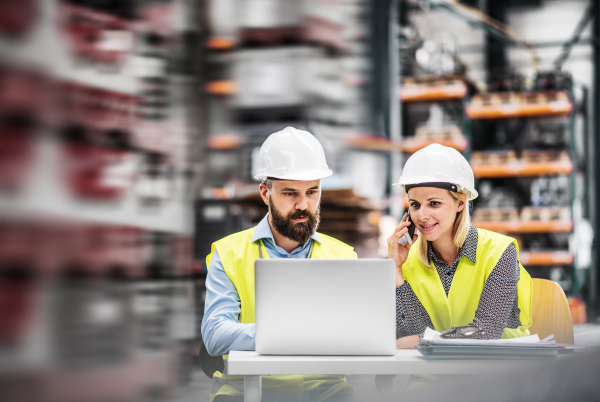 A portrait of a mature industrial man and woman engineer with laptop in a factory, working.