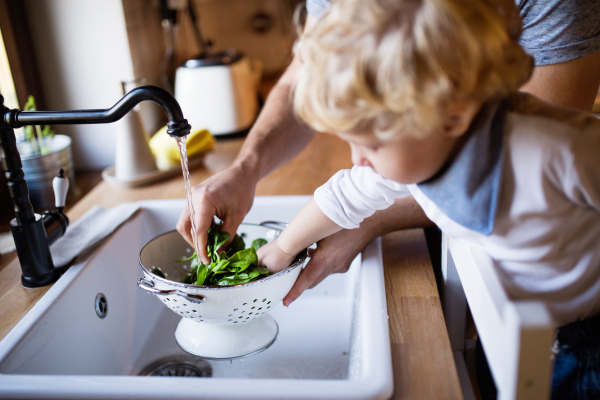 Unrecognizable young father with a toddler boy cooking. A man with his son making vegetable salad.